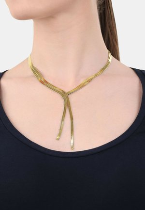 Goldene Metallkette mit einem V-förmigen Design, die aus zwei verlängerten Strängen besteht, die herabhängen und auf einem dunklen Rundhalsausschnitt-Oberteil ruhen.