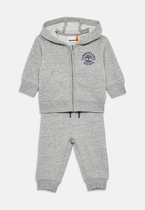 Grå bomulds baby tracksuit med en lynlås hoodie og bukser. Har ribbede manchetter, forlommer og en logo print på hoodien.