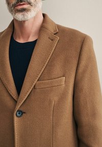 Bruine wollen blend jas met een notch lapel, enkele knoopsluiting en een opgestikte zak aan de linkerkant; gekorrelde stof met een zachte afwerking.