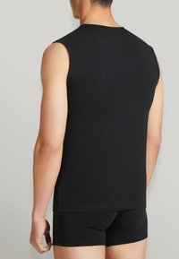 Top nero senza maniche realizzato in un tessuto liscio, con scollatura rotonda e design aderente. Abbinato a pantaloni boxer neri coordinati.