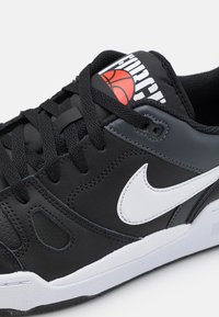 Sapatilha atlética preta com materiais sintéticos, swoosh branco da Nike, atacadores pretos, língua acolchoada com um logótipo vermelho de basquetebol, sola texturizada.