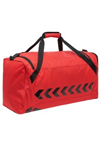 Sac de sport rouge en tissu, orné de graphiques de flèches noires sur un côté, avec deux poignées noires et une fermeture éclair en haut.