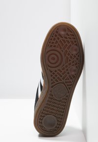 Suela de zapatilla negra con material de goma. Presenta patrones de agarre texturizados y diseños circulares. Destaca la marca Adidas en el talón.