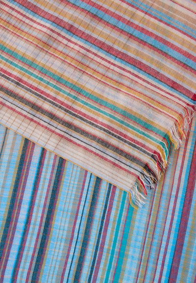 Υφαντό ύφασμα με πολύχρωμες οριζόντιες ρίγες σε κόκκινο, κίτρινο, μπλε, μαύρο και άσπρο, που δείχνει την υφή και τις περιθωριακές φούντες.