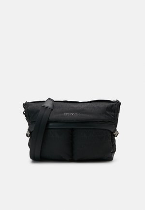 Sac bandoulière noir Emporio Armani avec design matelassé, sangle réglable et logo visible sur le rabat avant.