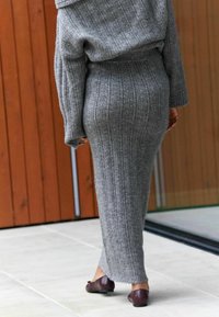 Graues, geripptes Strickkleid mit schulterfreiem Design, figurbetonter Silhouette und langer Länge, kombiniert mit dunkelbraunen flachen Schuhen.