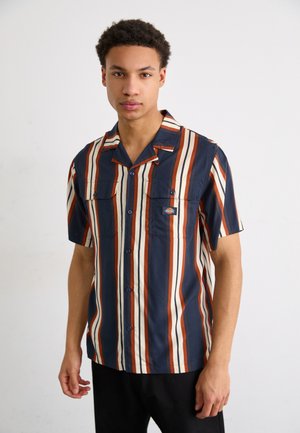 Camisa de(button-up) de manga corta a rayas en colores azul marino, crema y óxido. Cuenta con dos bolsillos en el pecho y un cuello tipo campamento. Tejido suave y ligero.