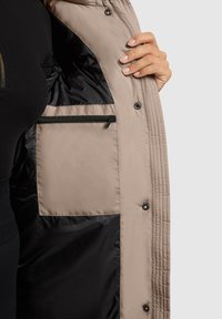 Bézs steppelt mintájú bélelt dzseki fekete belső béléssel és bal oldalon cipzáras zsebbel. Patentok láthatók.