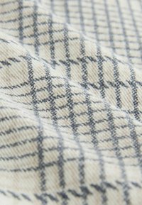 Kremfarvet stof med blød tekstur og et sort og gråt ternet mønster i diagonale folder.