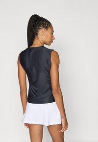 Μαύρο αθλητικό τοπ χωρίς μανίκια με εφαρμοστή γραμμή, ραβδωτή υφή και διακριτική κυρτή λεπτομέρεια ραφής στην πλάτη, σε συνδυασμό με λευκή φούστα.