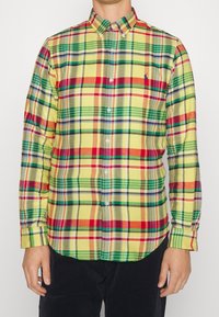 Karo košile v žluté, zelené, červené a modré barvě. Má límec na knoflíky a dlouhé rukávy s knoflíkovými manžetami. Bavlněná tkanina.