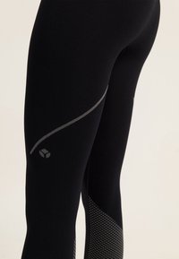 Mustat urheiluleggingsit, joissa on sileä kangas, heijastava harmaa raitakuosi ja teksturoitu verkkopaneeli alhaalla.