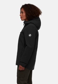 Schwarze wasserdichte Jacke mit Kapuze, mit Reißverschlusstaschen und einem Logo-Patch am Ärmel. Der Stoff hat eine glatte, matte Oberfläche.