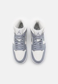 Ett par vita och grå högskor med snören, perforerade tånärare och "AIR"-logotyp på vadderade tungor, sedda ovanifrån.