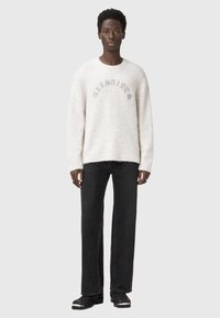 Suéter de color gris claro y esponjoso con "AllSaints" bordado en gris oscuro, combinado con jeans rectos negros y botas de tobillo negras.