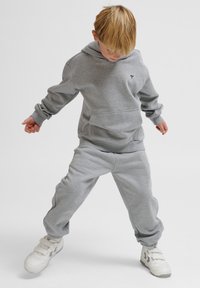 Graues Sweatshirt und Hose Set, mit einer vorderen Tasche, gerippten Bündchen und Logodetail, ergänzt durch weiße Sneakers.