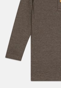 Brun ribbet langermet topp med knappestolpe. Myk tekstur med en tettsittende design. Inkluderer sømmer sydd i mansjetter og nederkant.