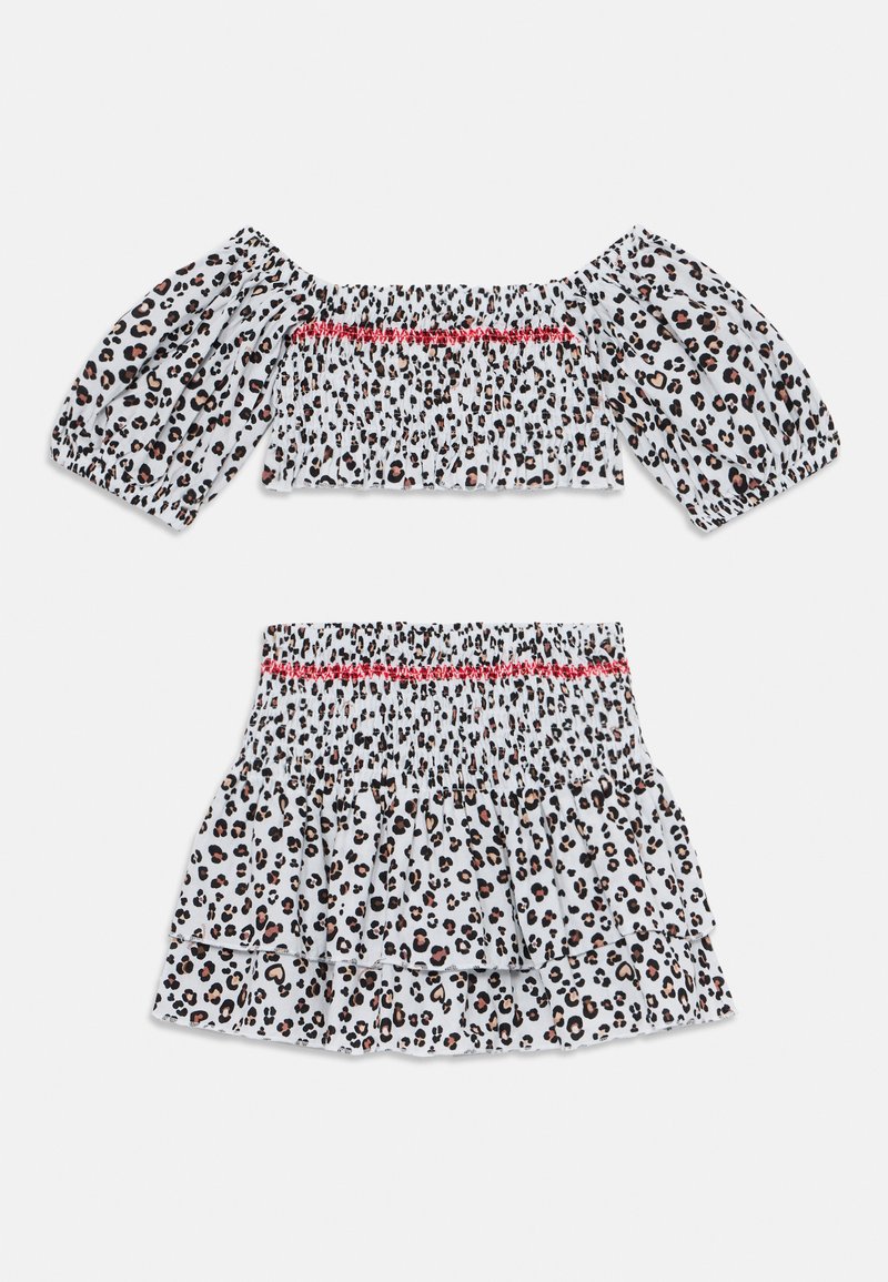 Completo a due pezzi con stampa leopardata, composto da un crop top smock off-the-shoulder con maniche a sbuffo e una mini gonna a campana abbinata. Sfondo bianco con macchie nere e marroni. Accento rosso sul top.