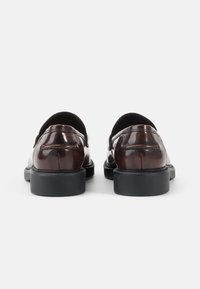 Bruine leren schoenen met een glanzende afwerking, ronde neuzen en een lage zwarte rubberen zool. Gemakkelijk aan te trekken zonder zichtbare sluitingen.