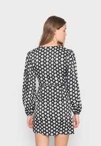 Vestido preto com padrão floral branco, mangas longas e bufantes, cintura ajustada e barra curta, apresentando um tecido suave e leve.