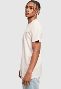 Lyserød bomulds t-shirt med rund hals, korte ærmer og et lille grafik på brystet. Bærer den med lys blå denim jeans.