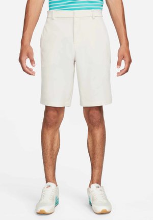 Pantalones cortos beige hechos de un tejido ligero, con un frente plano y una cinturilla estándar. Combinados con zapatillas blancas y una blusa a rayas.