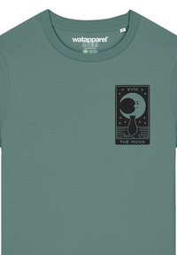 Türkises Baumwoll-T-Shirt mit Rundhalsausschnitt, versehen mit einem schwarzen Grafikdesign von einer Katze und einem Mond. Das Etikett zeigt die Marke "wat apparel."