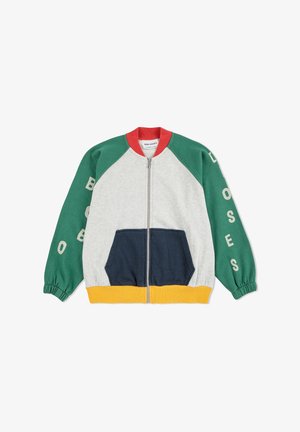Giacca colorata con zip, corpo grigio, maniche verdi, tasca frontale blu navy e orlo giallo. Presenta un design raglan e testo stampato sulle maniche.