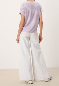 Camiseta de rayas en tono púrpura claro con mangas enrolladas, combinada con pantalones anchos de lino blanco, con un corte holgado y un sutil detalle de bolsillo trasero.
