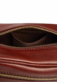 Interieur van een bruin leren tas met een ritsopening, voorzien van een klein stoffen vakje binnenin. Gouden ritsbeslag en stikdetails zichtbaar.