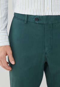 Pantalon en coton vert à coupe droite, équipé d'une fermeture à boutons et d'une texture lisse. La ceinture présente une texture légèrement rugueuse.