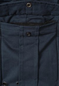 Navy fabric with a smooth texture. Features a vertical pocket, buttoned flap, and gold accents at the snap buttons.