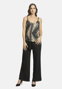 Top sin mangas en negro y beige con un patrón de hojas de palma, combinado con pantalones de pierna ancha negros y zapatos de tacón altos negros.