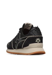 Sneaker in suede nera con suola beige, dotata di un logo e dettagli bianchi. Il design include una tomaia testurizzata e un colletto imbottito.