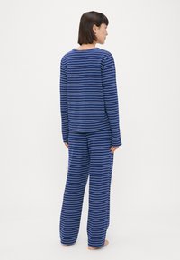 Dlhý rukáv, pyžamo v námorníckej modrej a bielej prúžkovanej vzore s voľným strihom a širokými nohavicami vyrobené z mäkkej látky.