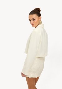 Witte cropped blazer met een kraag en lange mouwen, gecombineerd met een glinsterende, paillettenbeige minirok.