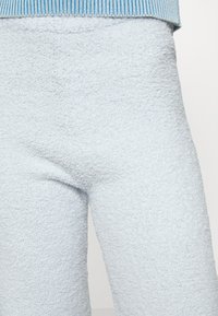 Calças de polar azul claro com uma superfície suave e texturizada e uma cintura canelada em uma faixa azul contrastante.