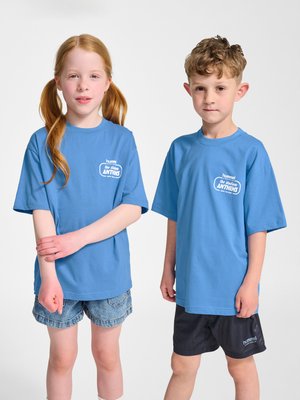 Twee kinderen staan zij aan zij en dragen bijpassende blauwe T-shirts van 'The Stadium Anthems', de een met spijkershorts en de ander met zwarte shorts.