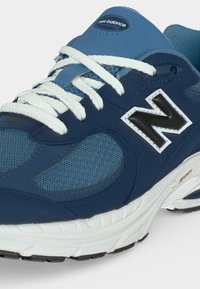 Μπλε και ναυτικό αθλητικό παπούτσι New Balance με λευκά κορδόνια, εμφανές μαύρο-άσπρο λογότυπο "N" και λευκή επενδεδυμένη σόλα με μαύρη σόλα.