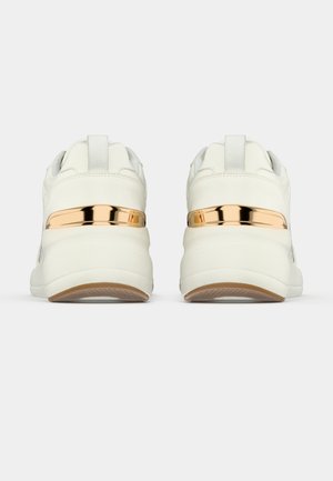 Paar weiße Sneaker von hinten mit metallisch goldenem Streifendetail über dicken weißen Sohlen auf einfachem Hintergrund.