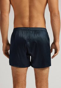 Tmavě modré plavkové šortky s elastickým pasem, vyrobené z hladké, lesklé tkaniny. Šortky mají volný střih a jednoduchý design.