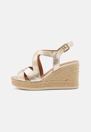 Złote metaliczne sandały na koturnie z krzyżującymi się paskami, odkryty czubek i regulowany pasek na kostce. Jutowy splot na pięcie.
