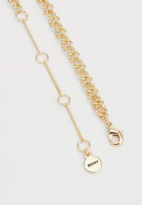Gold chain necklace featuring large round links, a lobster clasp, and a circular tag engraved with "DKNY." Smooth texture and polished finish.