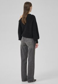 Sort striktrøje med løs pasform og dropped shoulder-detalje, parret med grå højtaljede lige jeans. Glat tekstur, minimalistisk design.