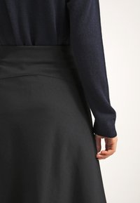 Falda negra, hasta la rodilla, con una textura suave y cintura ajustada. Un suéter de manga larga azul oscuro parcialmente visible. Diseño simple, sin patrones.