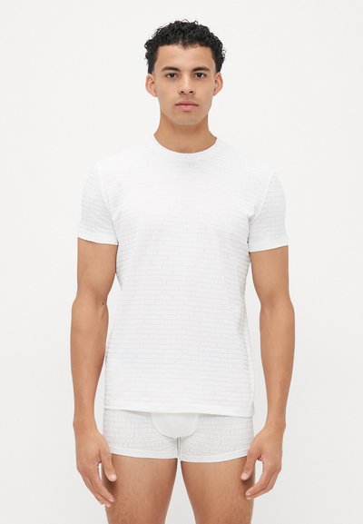 Weißes T-Shirt mit kurzen Ärmeln und subtilen Logo-Design, kombiniert mit passenden weißen Boxershorts. Beides verfügt über eine glatte, weiche Textur.