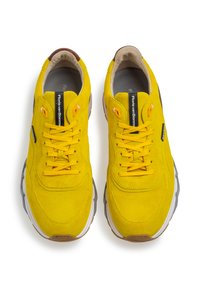 Gula sneakers med övre i mocka och mesh, vadderad krage, gummisula, snörningsdesign och reflexdetaljer på sidorna.