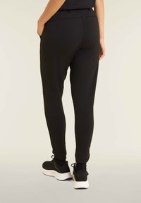 Pantalons de jogging noirs en tissu doux, avec une coupe slim, une taille élastique, des poches latérales et des chevilles resserrées. Portés avec des baskets noires.