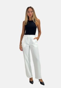 Zwarte mouwloze bodysuit, witte op maat gemaakte broek met voorkantzakken en zijknopen, gladde textuur, model draagt zwarte hakken.