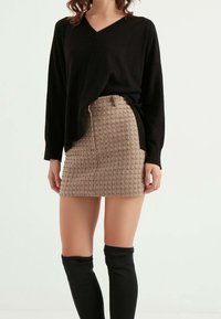 Maglione nero a scollo a V abbinato a una minigonna beige testurizzata con motivo a griglia, completato da lunghi calzini neri.